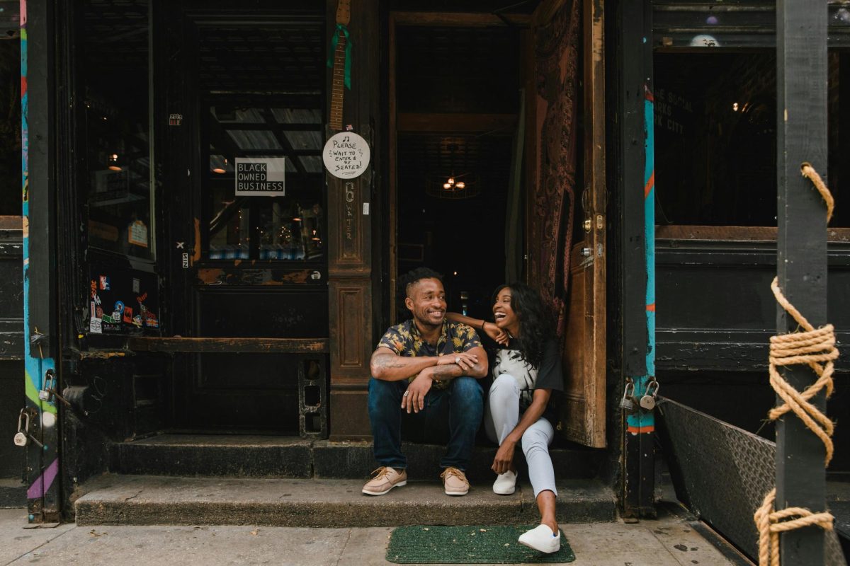 Two smiling owners sitting in front of their cafe. 